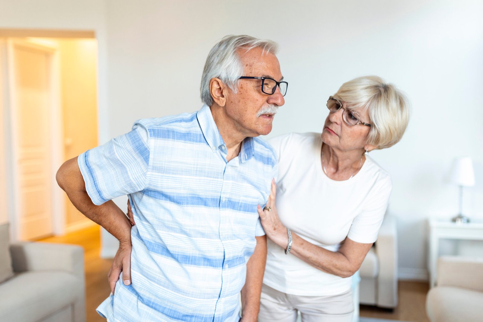senior couple homeelderly man is having back pain his lovley wife supports him scaled