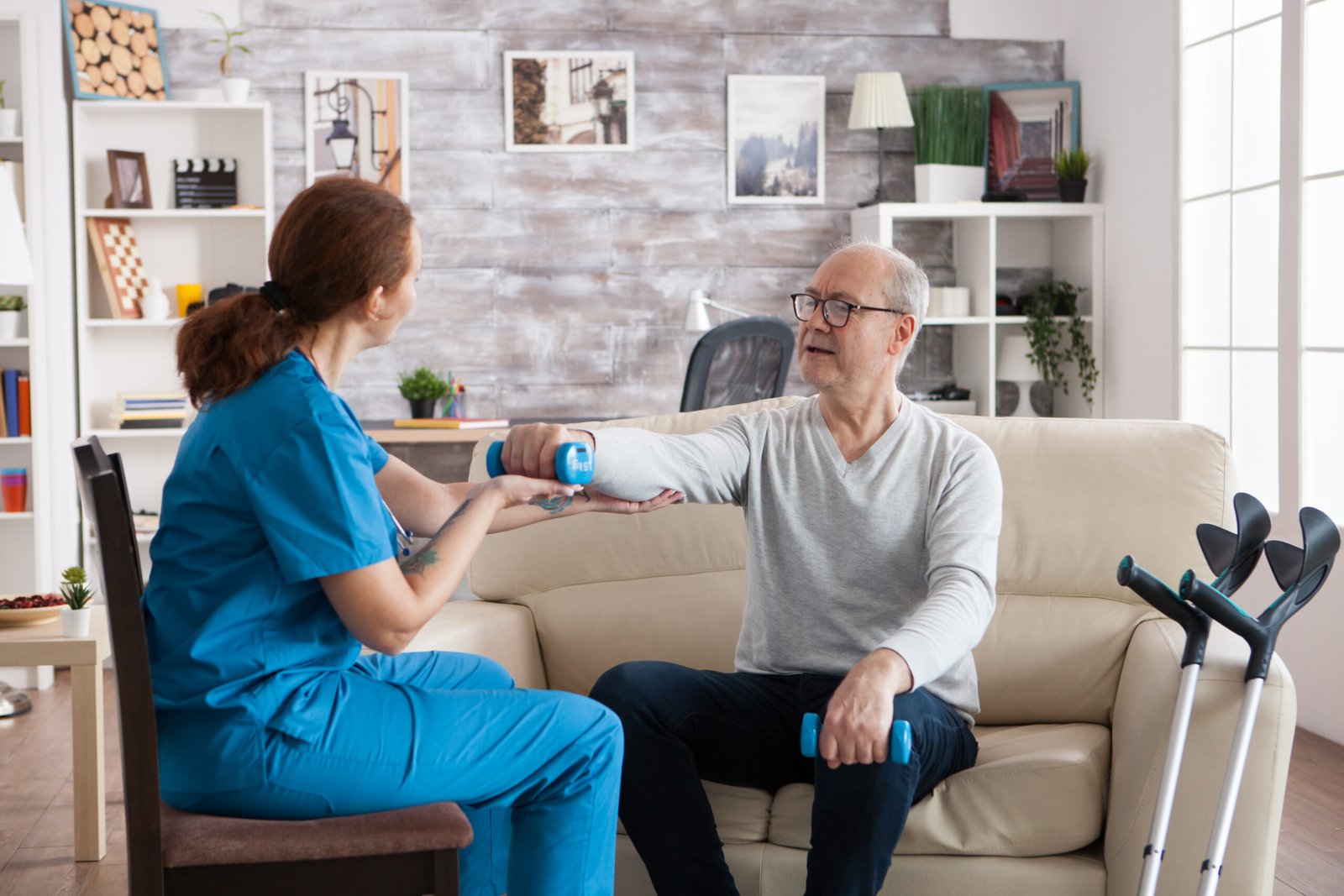 young nurse doing physiotherapy treatment nursing home with senior man using dumbbells scaled