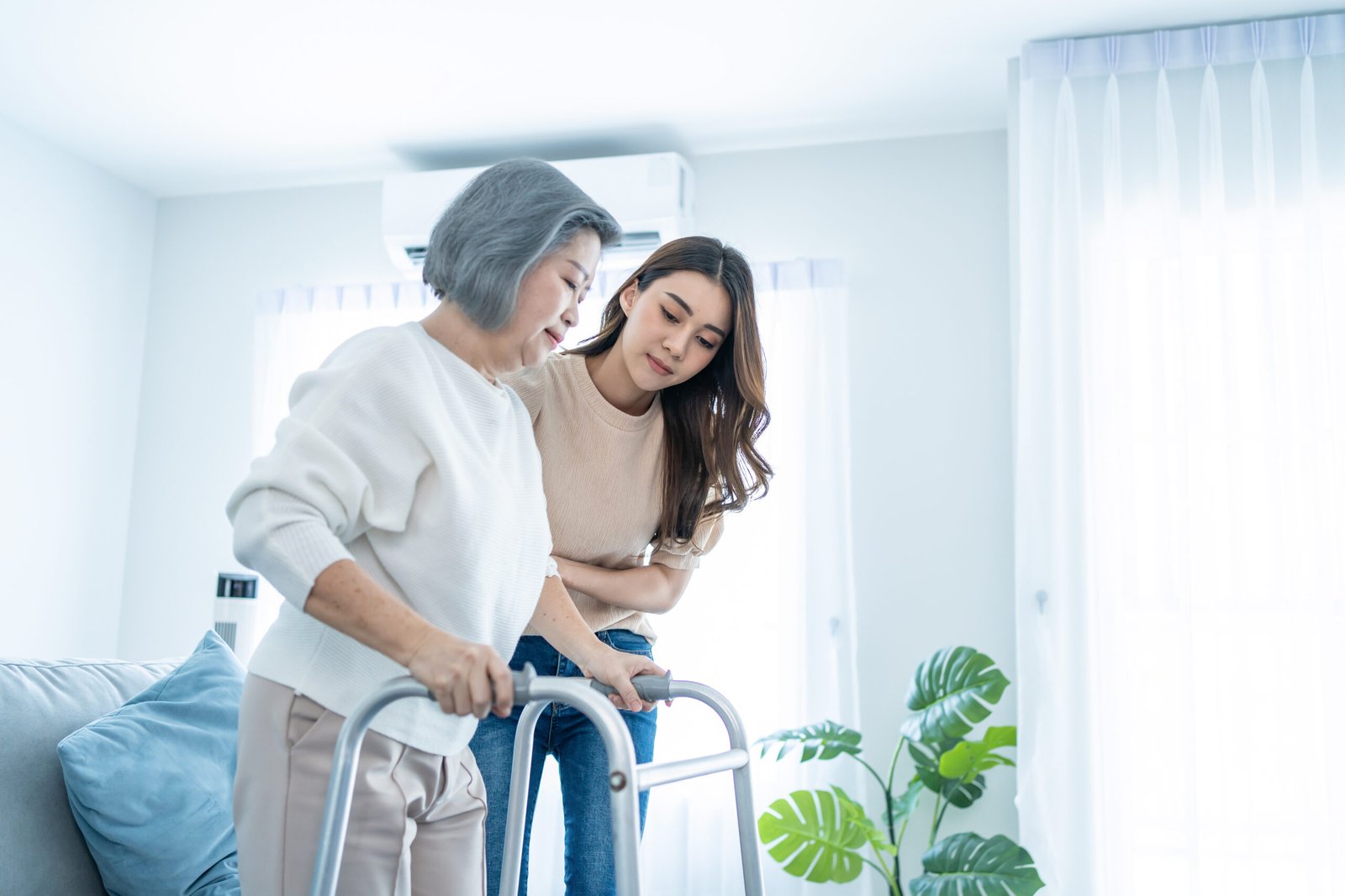asian daughter support older woman grandma walk with walker home beautiful girl help take care senior elderly mature mother patient stand doing physical therapy living room house scaled