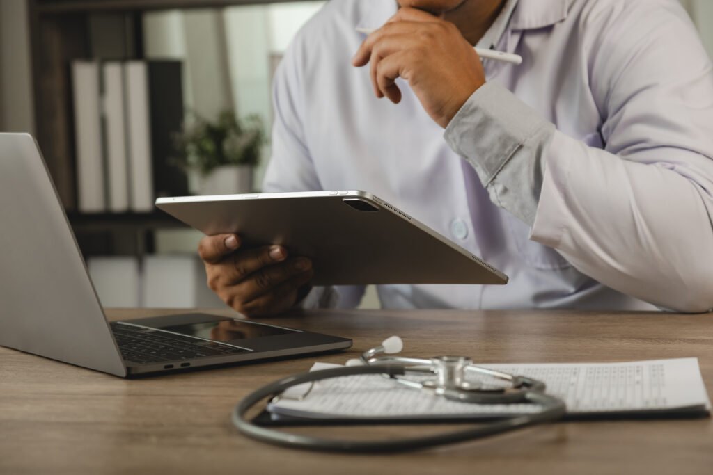 healthcare professional reviewing patient records tablet beside laptop stethoscope 1