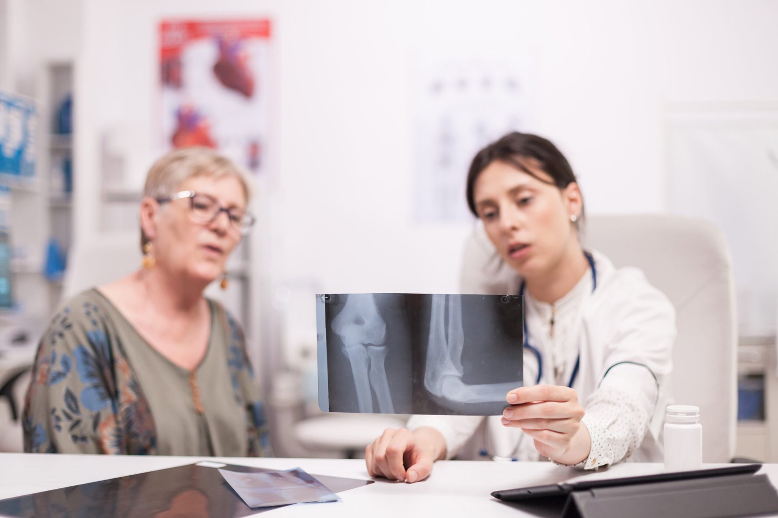doctor holding x ray talking with senior patient about knee injury hospital office medic talking about therapy with mature woman scaled