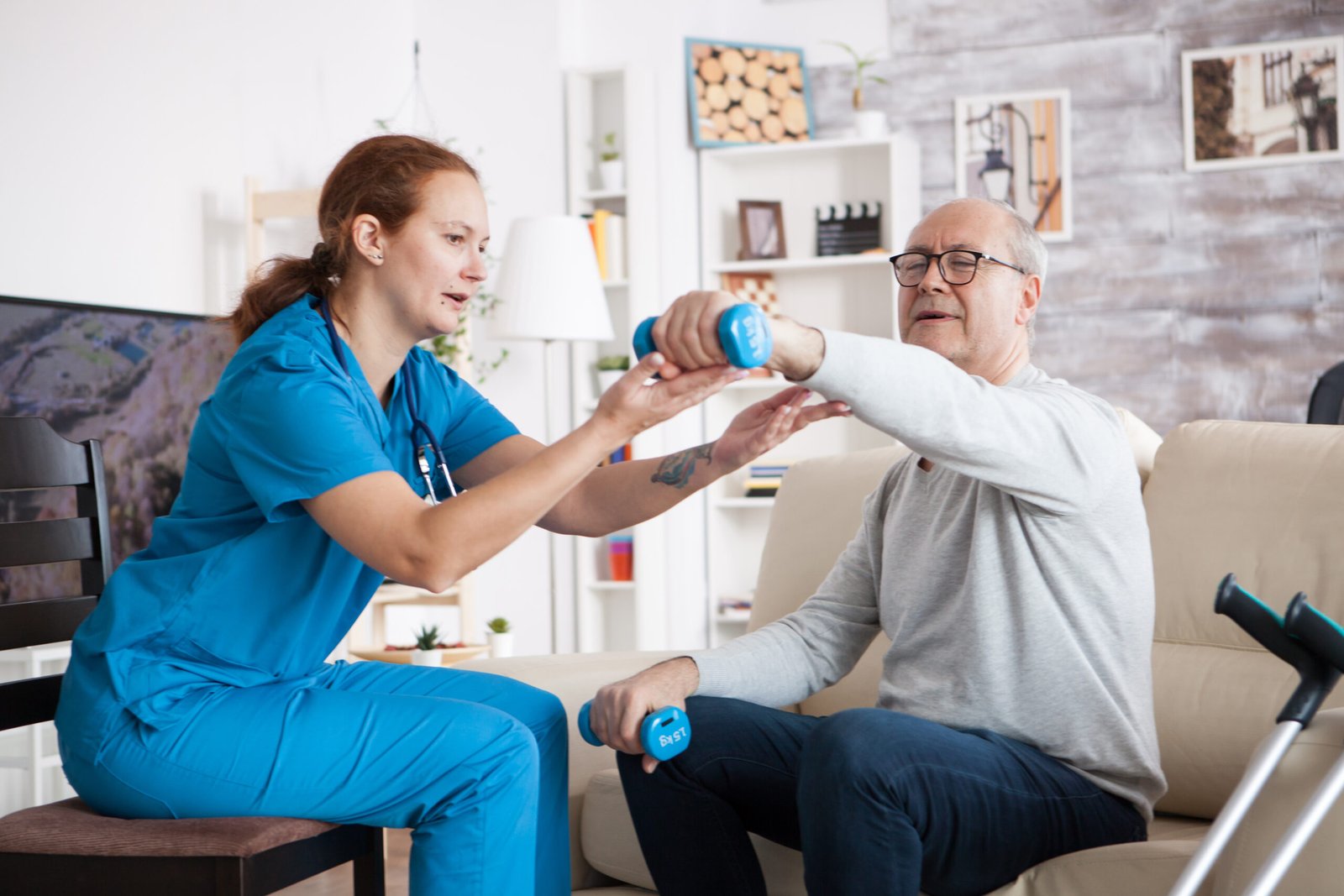 senior man nursing home with doing physical therapy with help from nurse using dumbbells scaled