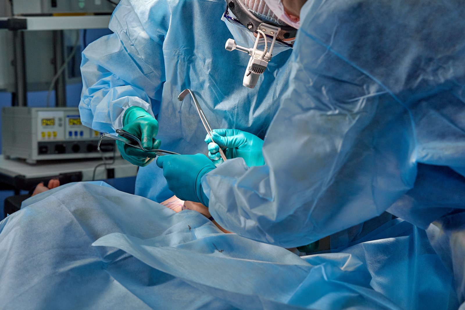 surgeon performing cosmetic surgery hospital operating room surgeon mask wearing loupes medical procadure breast augmentation enlargement enhancement blue background blue filter scaled